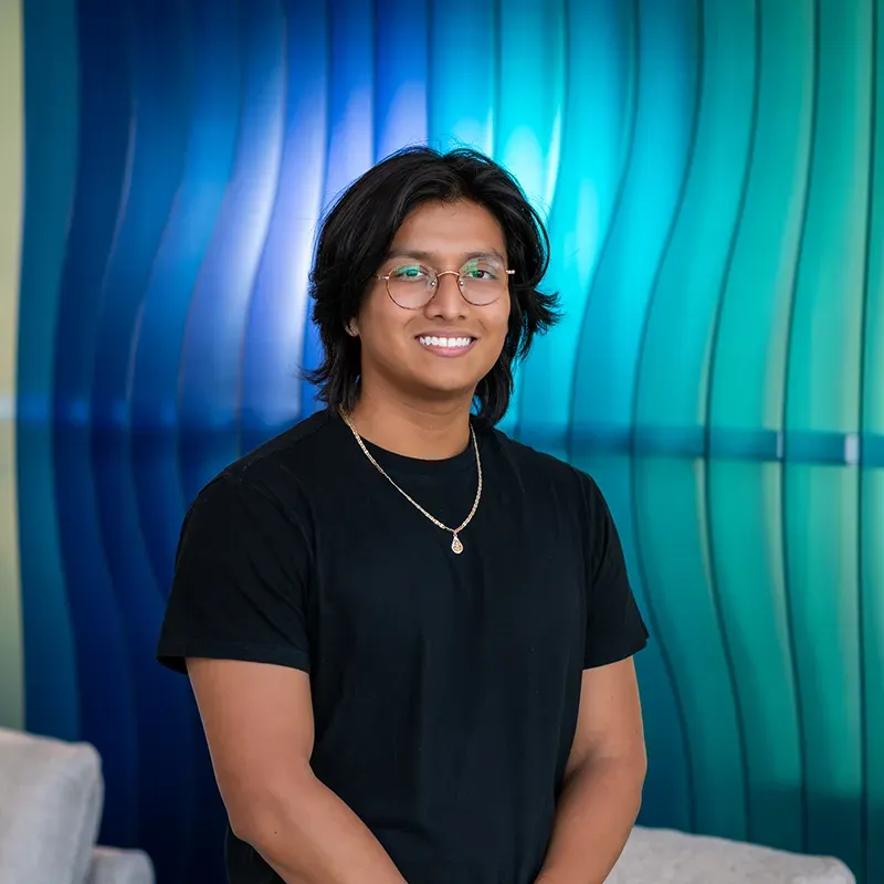 Person in glasses and black shirt smiling against a blue abstract wall