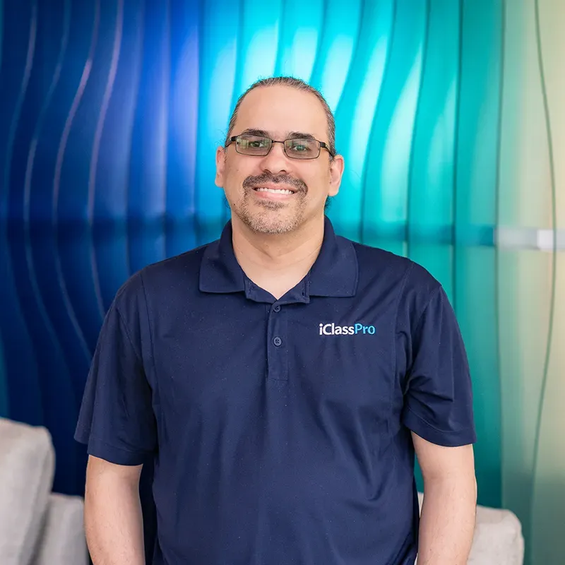 Smiling person in a navy polo standing before a blue and teal wavy backdrop