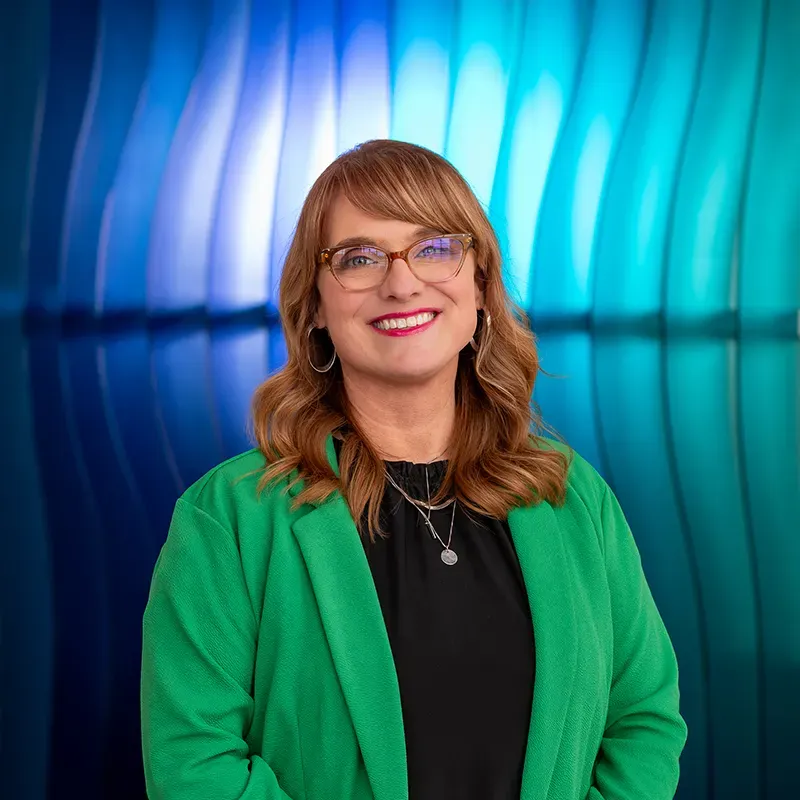 Smiling person in green blazer before a blue and teal abstract background