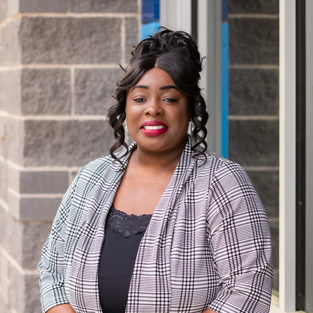 Smiling woman in a plaid blazer standing by a stone building wall
