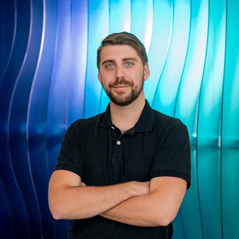 Man in a black polo with arms crossed, standing against a blue and turquoise abstract wall