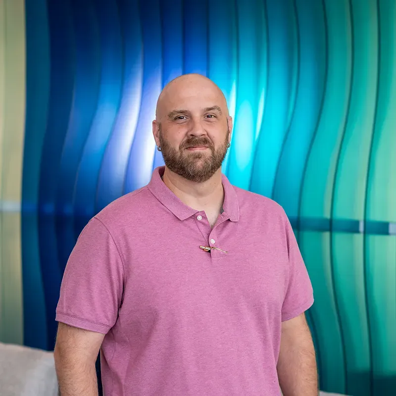 Man in a pink polo shirt standing against a blue-green wavy backdrop