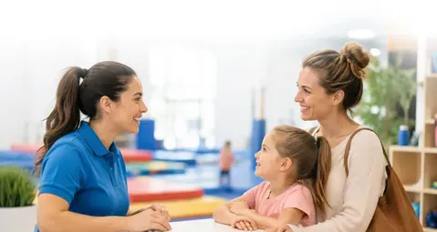 Two women and a child talking at a colorful table in a bright indoor setting