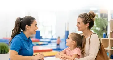 Two women and a child talking at a colorful table in a bright indoor setting