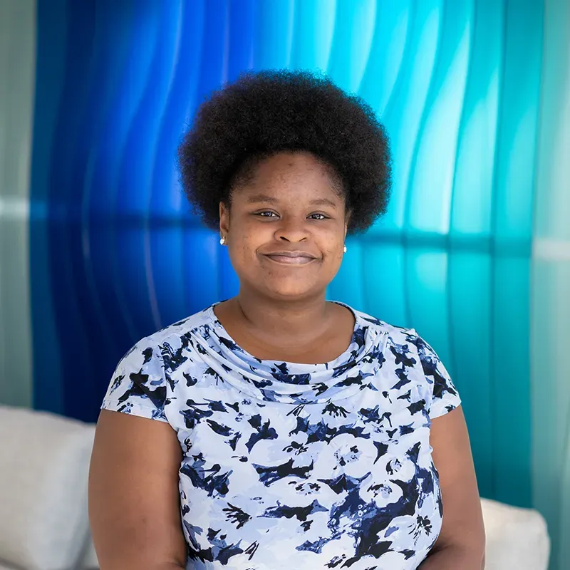 Person smiling against a blue and teal backdrop, wearing a white and navy patterned shirt