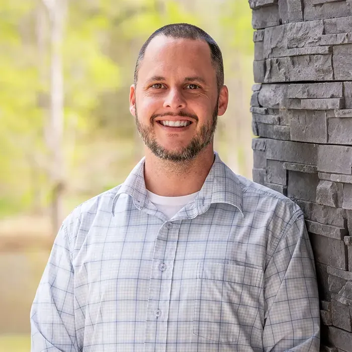 A person with a beard, wearing a light blue and white checkered button-down shirt