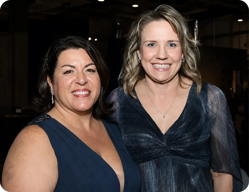 Two women smiling at an indoor event, both in dark formal dresses.