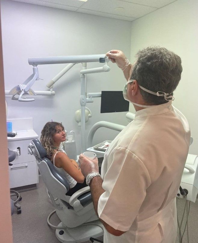 Dentist in white coat examines a woman in a dental chair in a clinic.