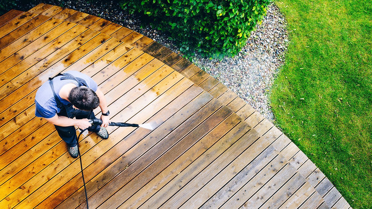 Overhead view of a person aiming a rifle on a wooden deck beside green grass and shrubs