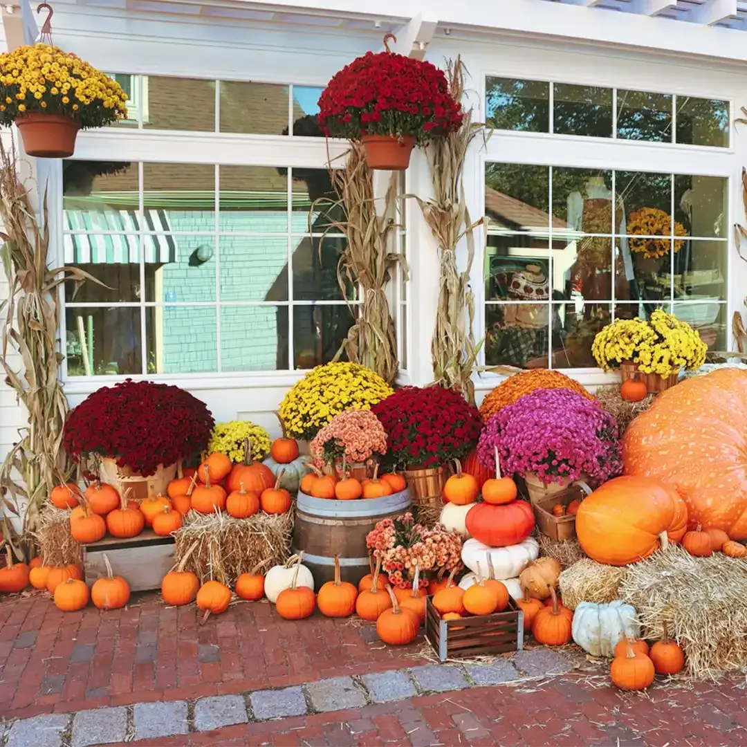 Autumn porch display with pumpkins, hay bales, and colorful mums in front of windows