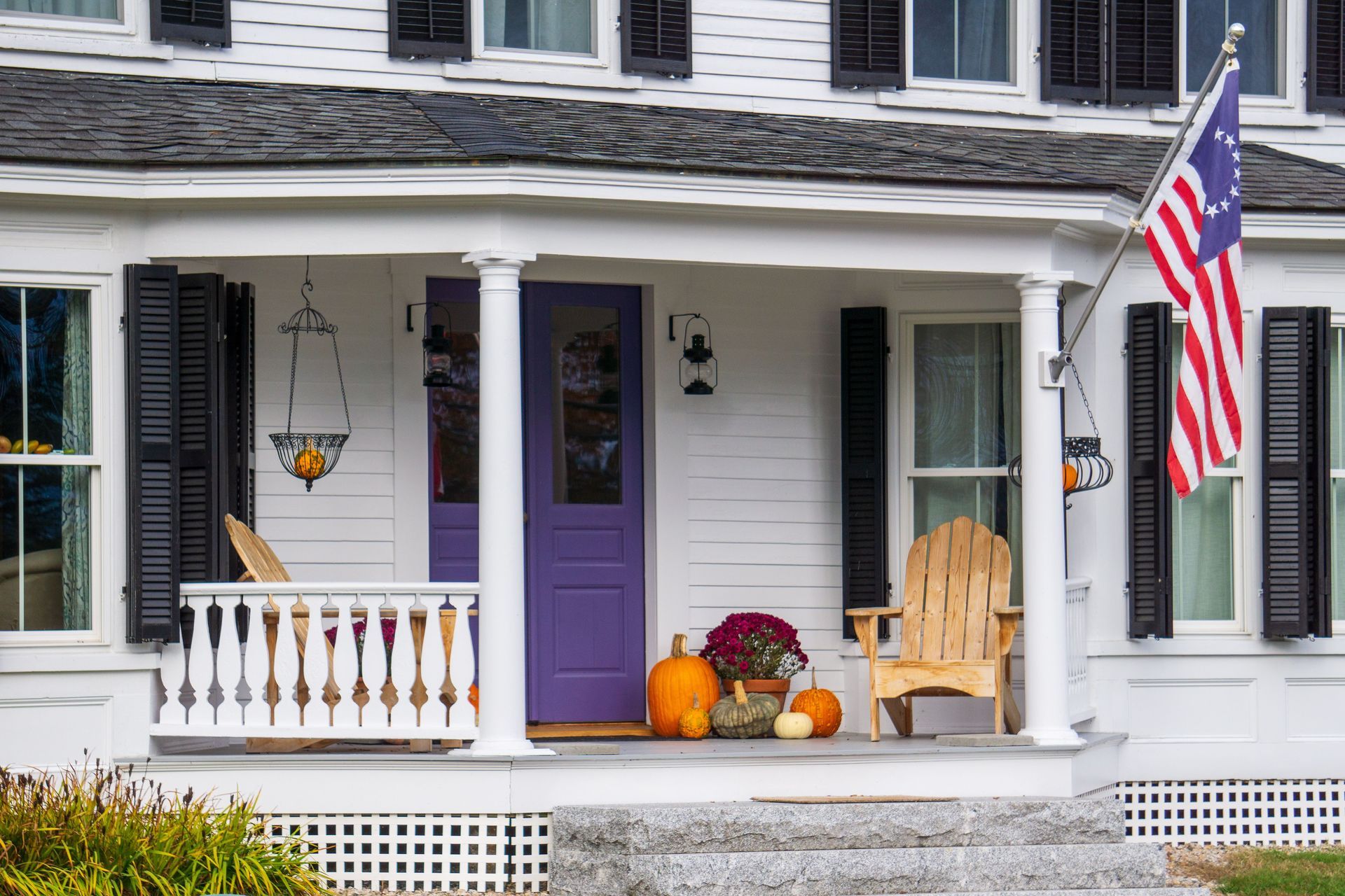 White house porch with purple door, autumn decorations, and an American flag