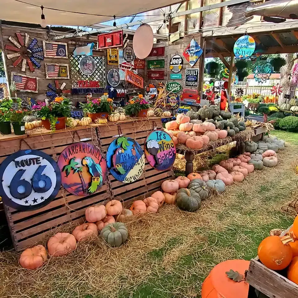 Colorful pumpkin display with painted signs and autumn decorations at an outdoor market booth