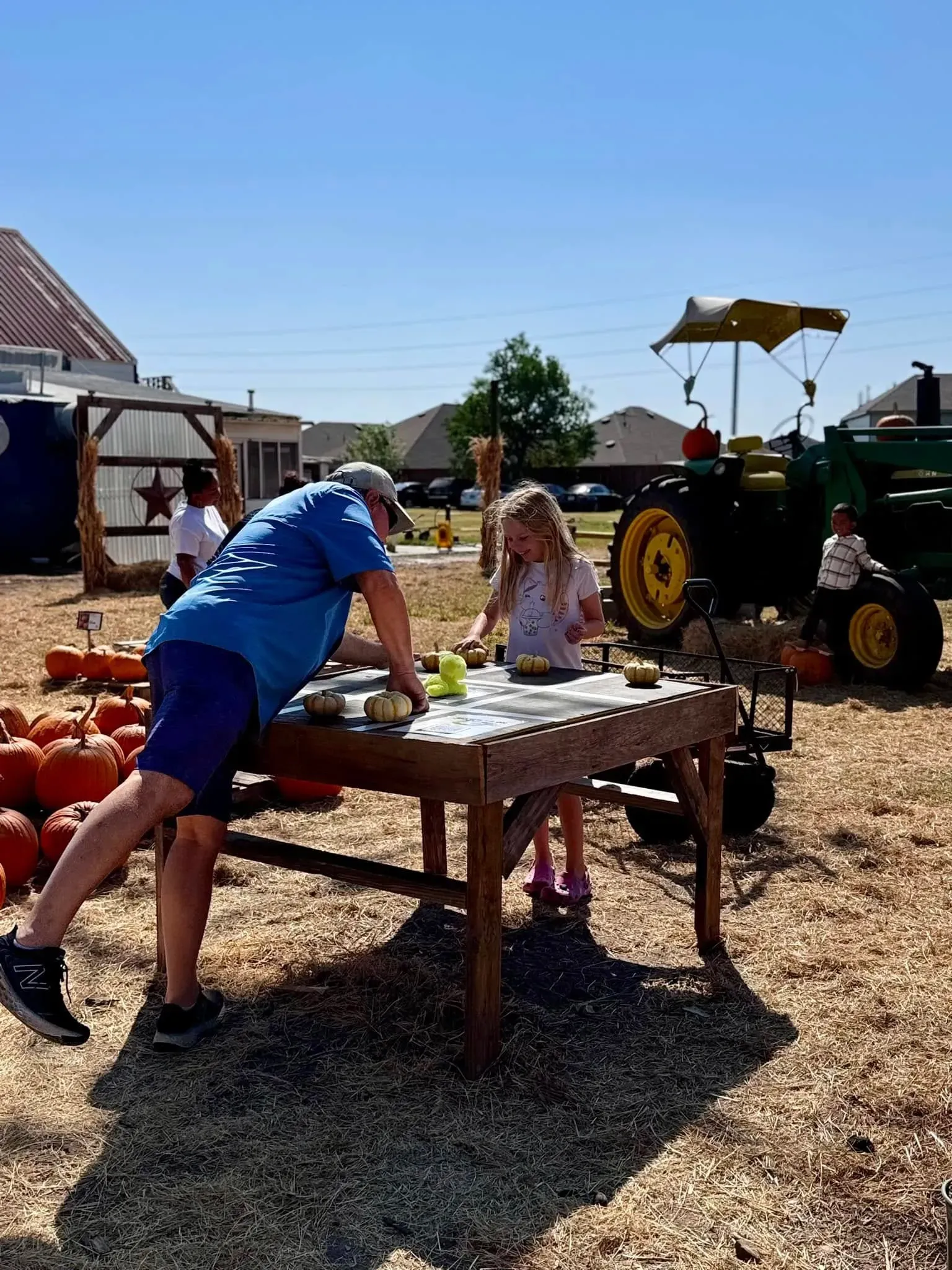 People playing on a wooden table outdoors at a farm event, with a tractor in the background.