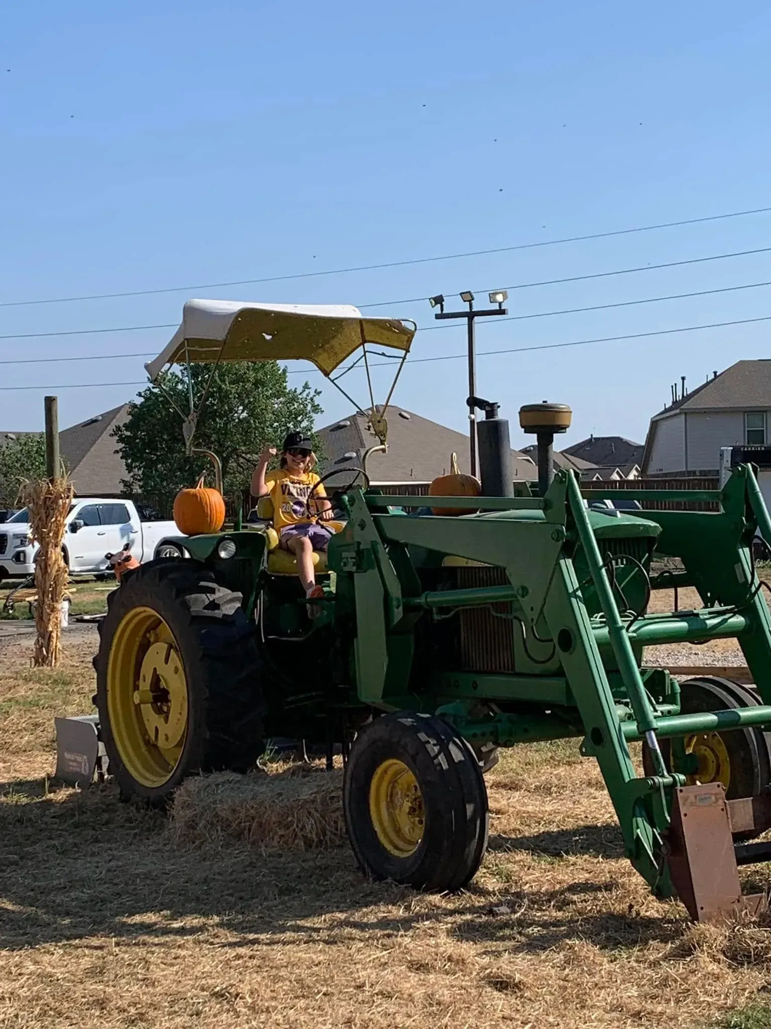 Green tractor with front loader carrying people at a farm event under a clear sky