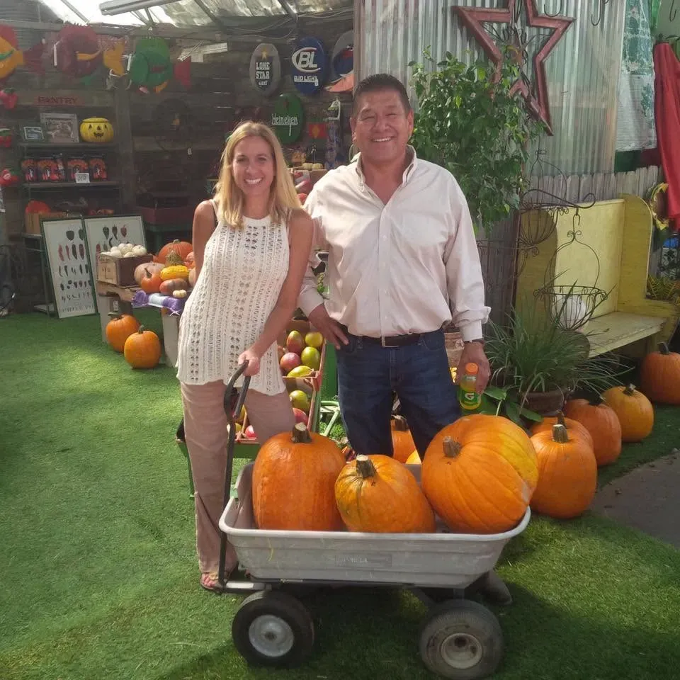 Two people standing by a wheelbarrow of pumpkins at a pumpkin patch display.