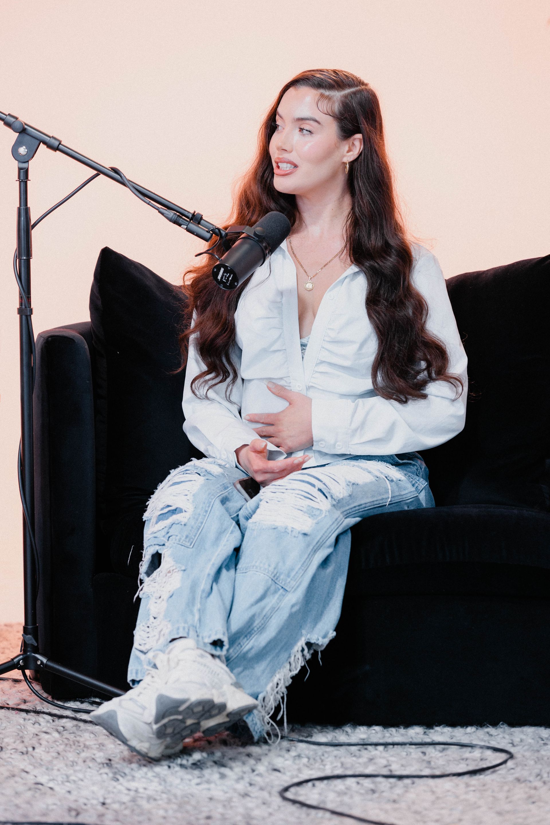 Woman seated on a black couch, speaking into a microphone during a podcast interview.