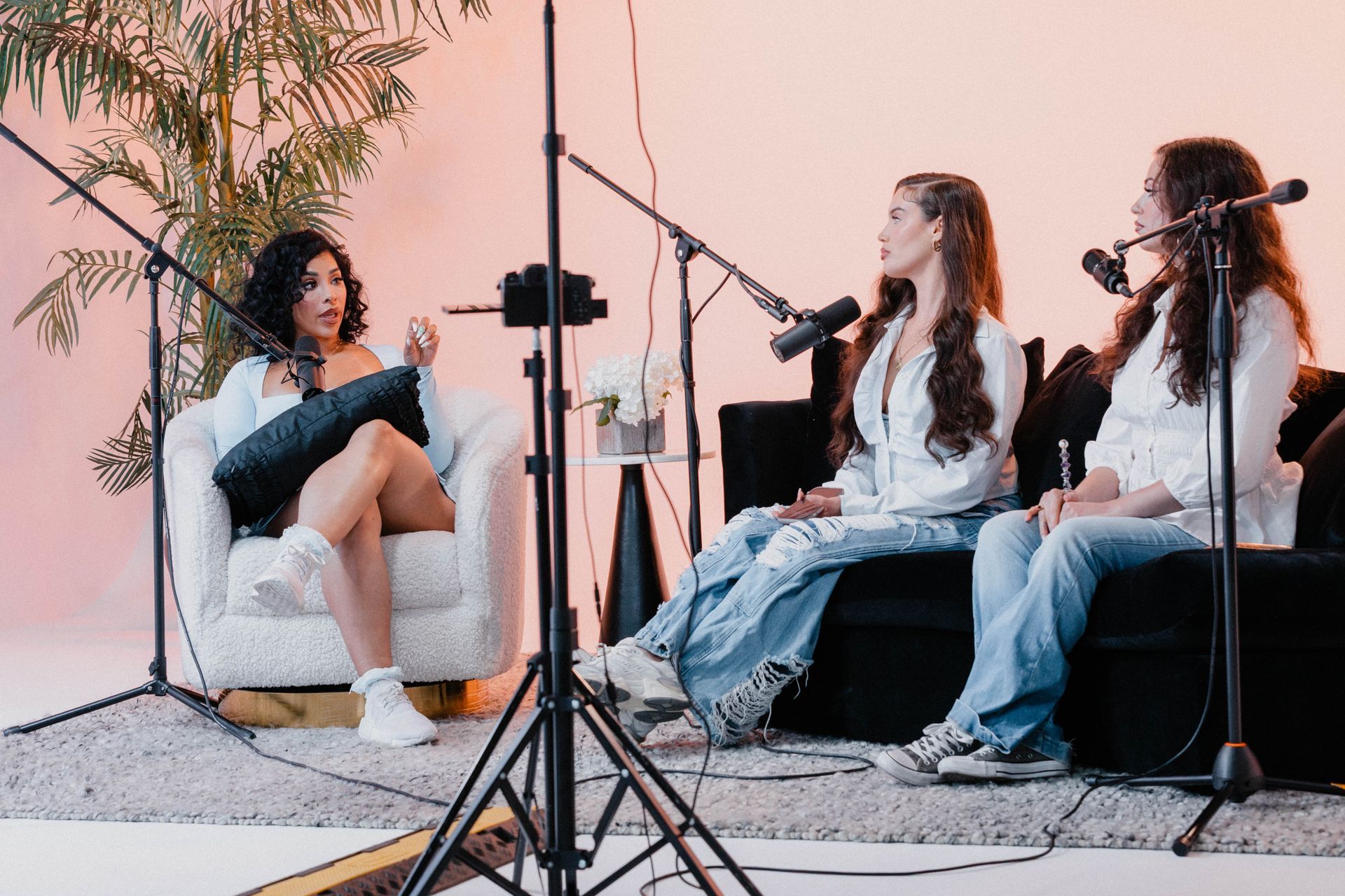 Three people recording a podcast on couches with microphones and studio equipment in a cozy indoor setting