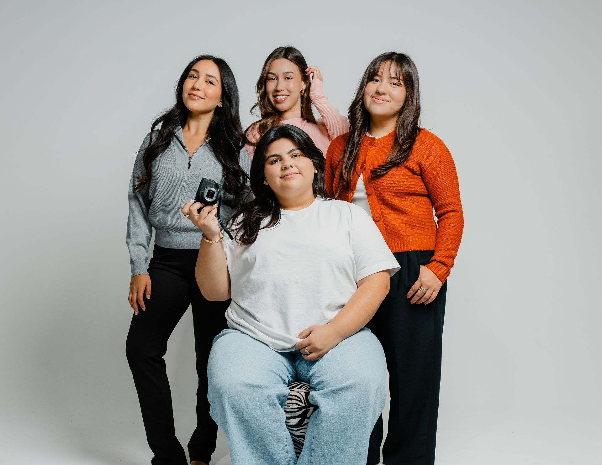 Four people posing in a studio, smiling, with one seated in front and three standing behind.