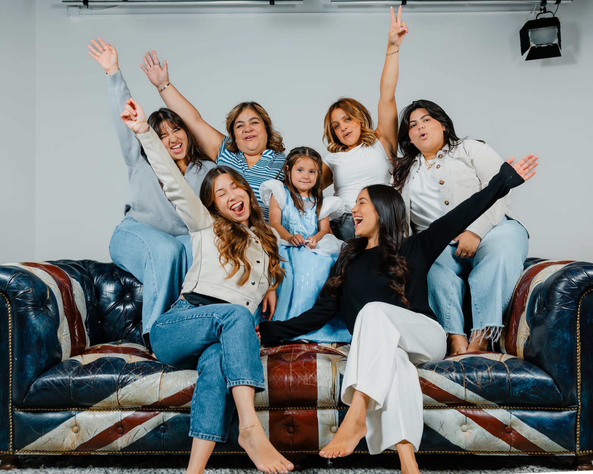 Group of people sitting on a blue leather couch, smiling and raising their arms in a bright living room.