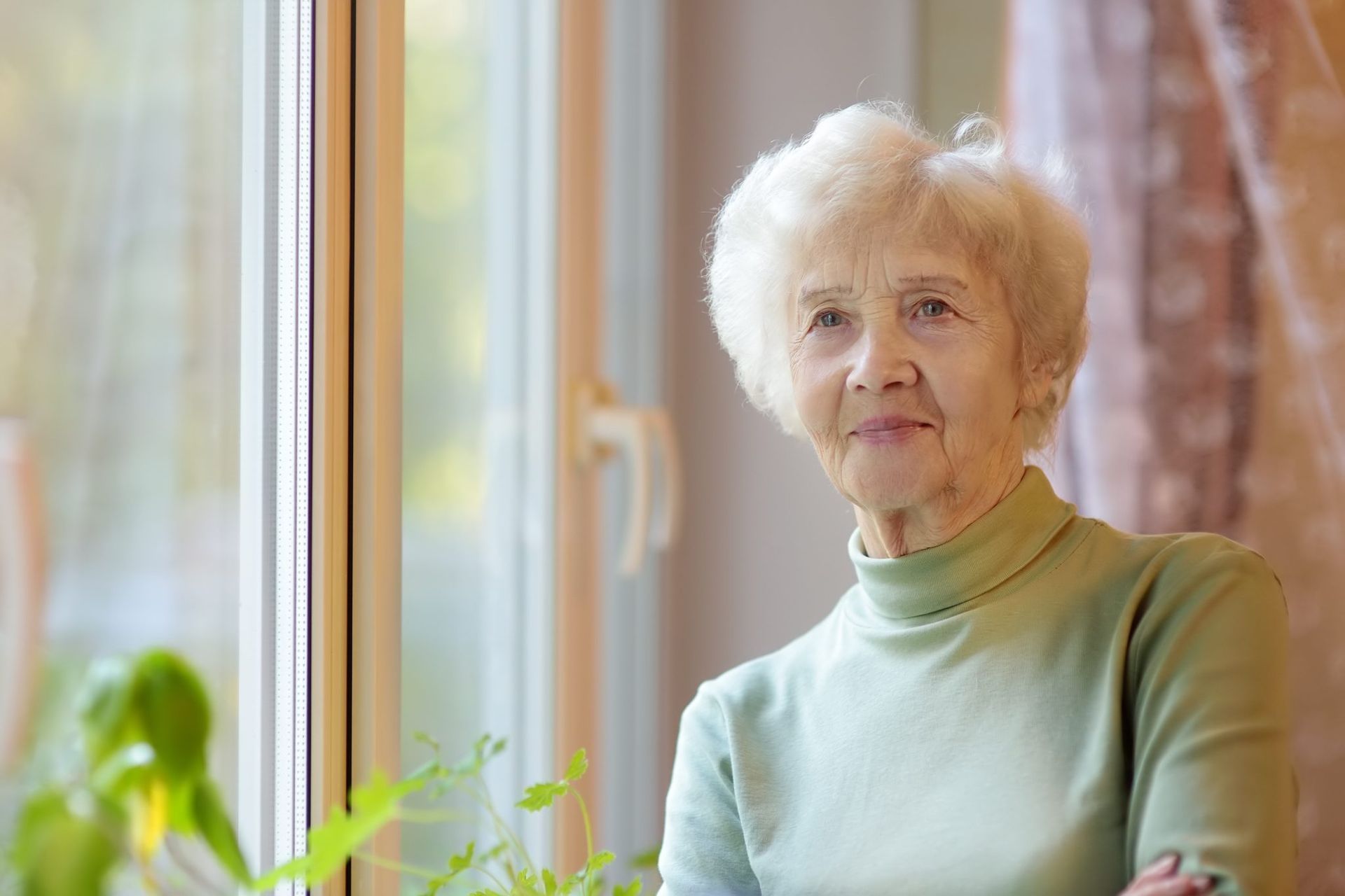Older woman in a mint sweater by a sunlit window with potted plants