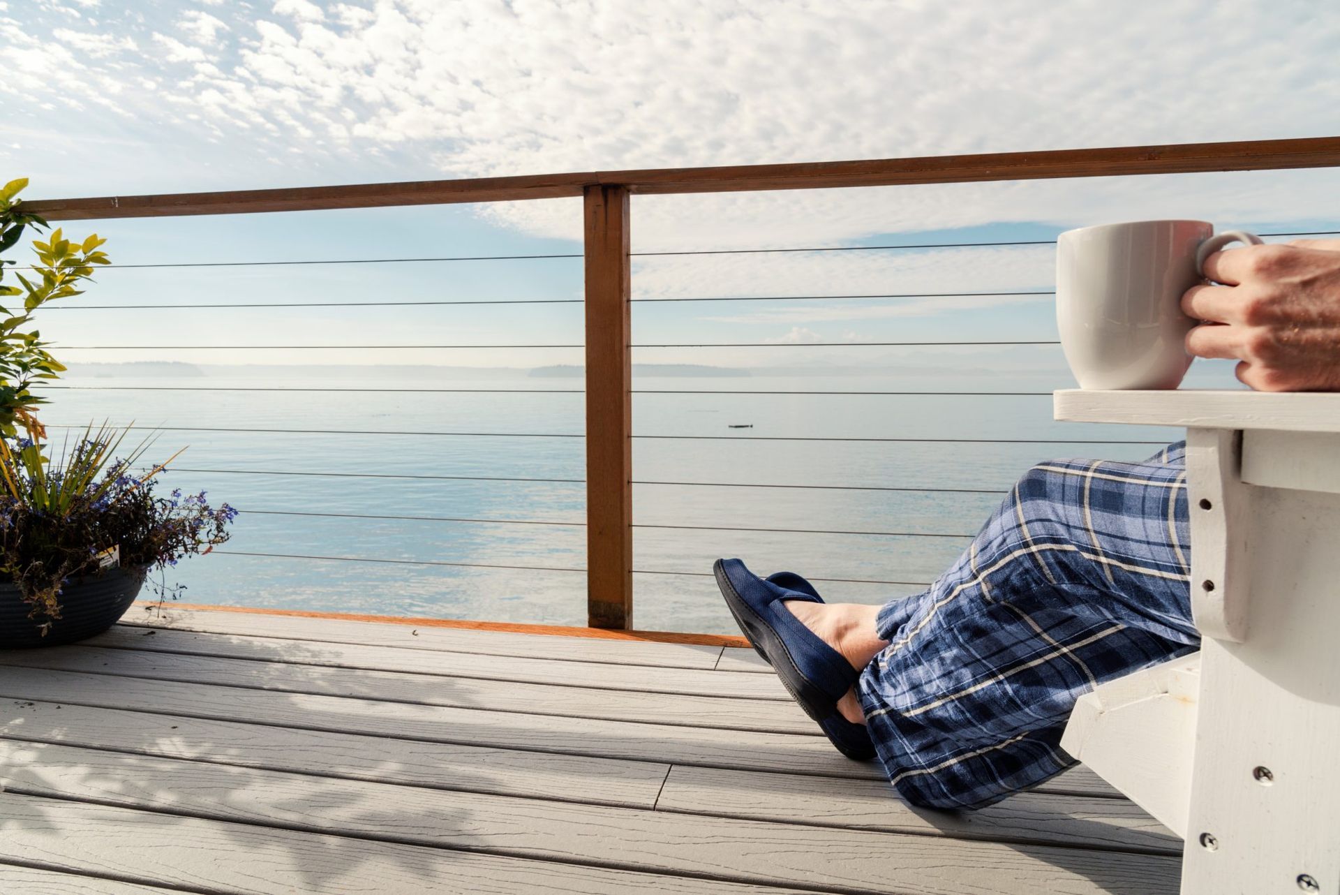 Person relaxing in blue plaid pants on a deck chair, looking out over a calm ocean at sunset