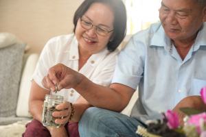 Two people smiling while opening a glass jar on a couch, with a pink flower in the foreground