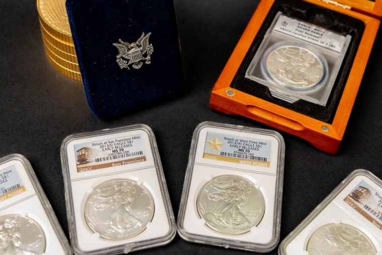 Graded silver coin slabs displayed on a dark surface, including one in an orange case and others in white holders