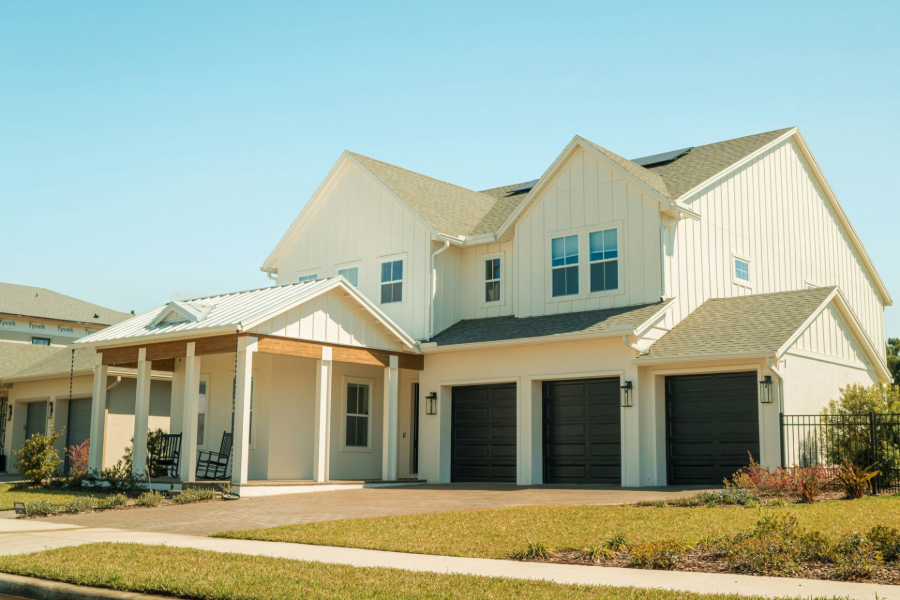 Two-story beige suburban house with a front porch and garage under a clear blue sky
