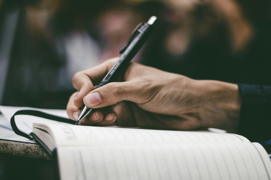 Hand writing in a notebook with a black pen on a table