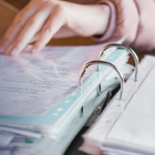 Hands turning pages in a binder with clear plastic rings on a desk