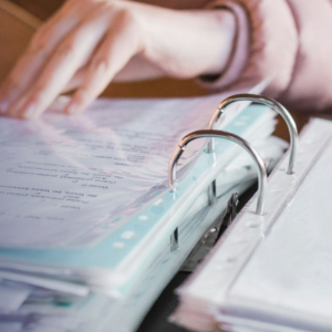 Hands turning pages in a binder with clear plastic rings on a desk