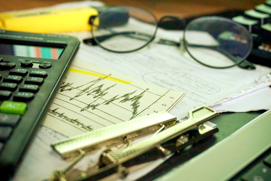 Calculator, eyeglasses, and pen on financial charts and papers on a desk
