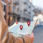 Hand holding a smartphone over a map with red location pins marking destinations