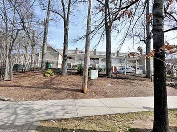 A row of houses are surrounded by trees and a sidewalk.