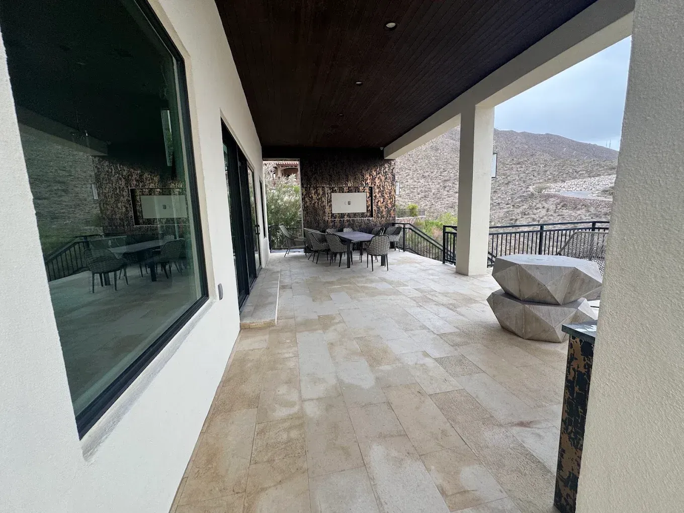 Covered patio with beige stone flooring, outdoor seating, and mountain views beyond columns