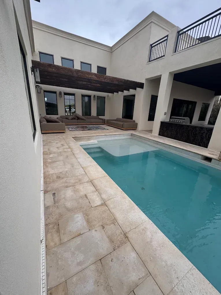 Courtyard pool beside a modern white villa with lounge chairs and covered patio