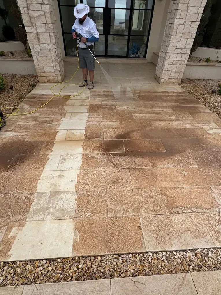 Person pressure-washing a stone patio in front of a house entrance.