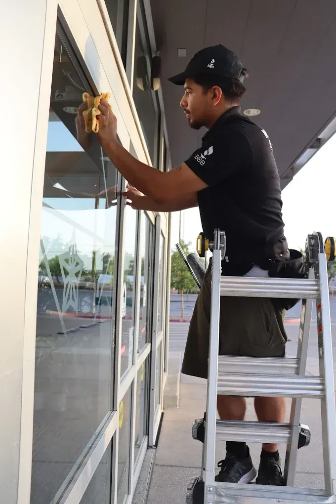 Worker cleaning glass storefront window from a ladder outdoors
