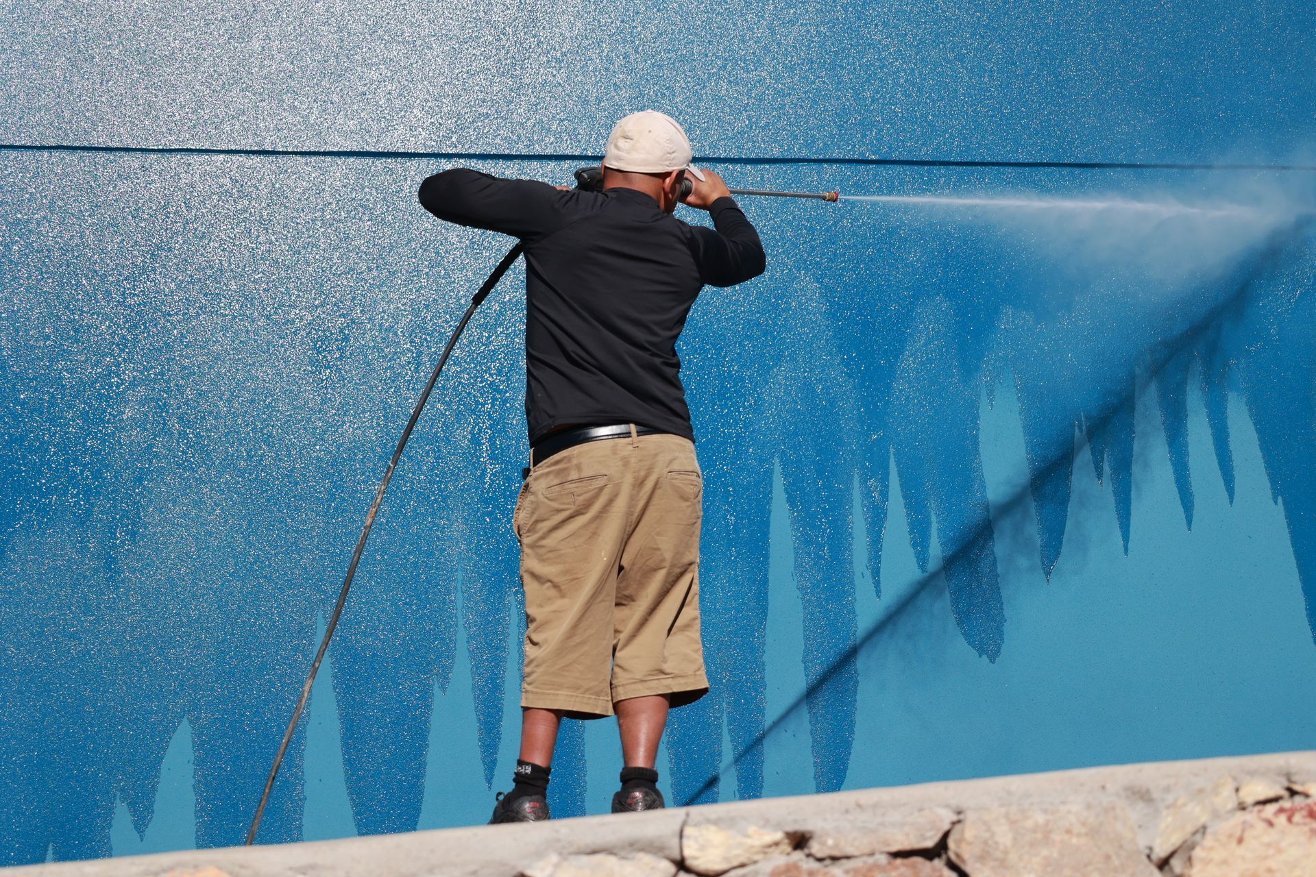Person spraying water on a blue wall with a hose from a stone ledge