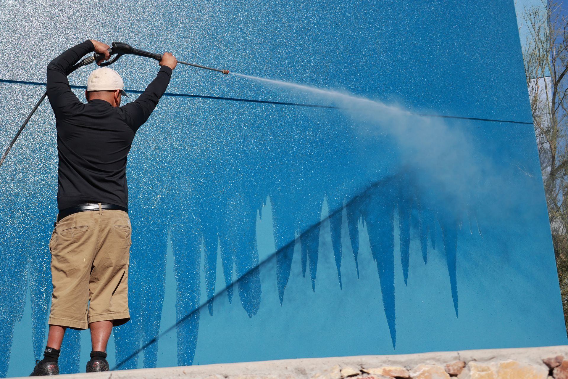 Person spraying water on a large blue wall, creating a diagonal stream and wet streaks