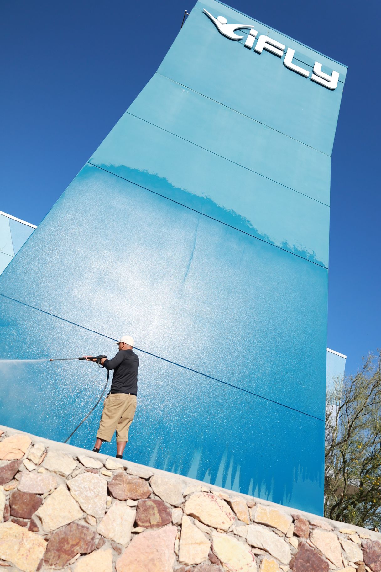 Person standing on rocks pointing toward a tall blue APU sign against a clear sky