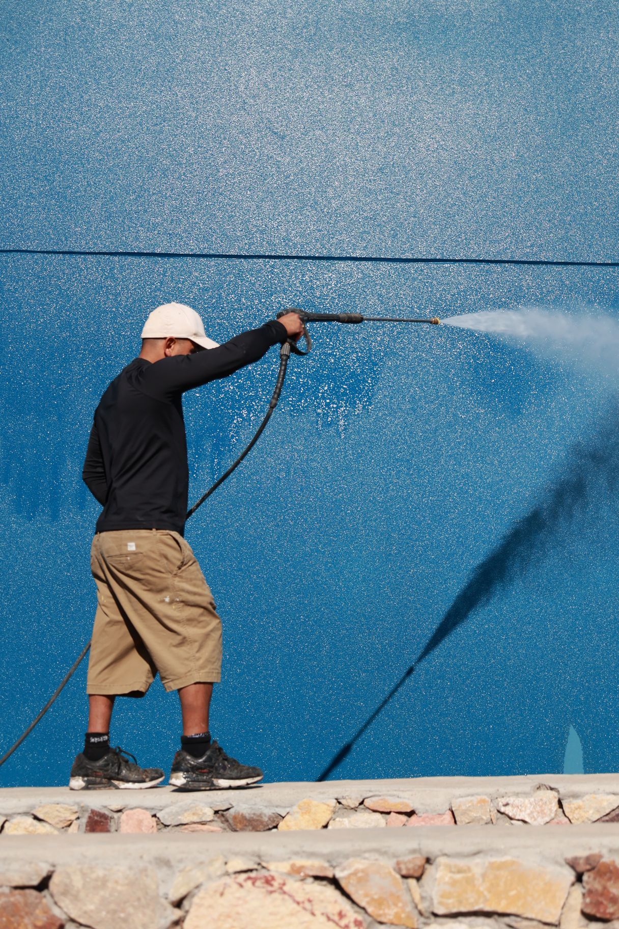 Worker pressure-washing a blue wall, spraying water across the surface.