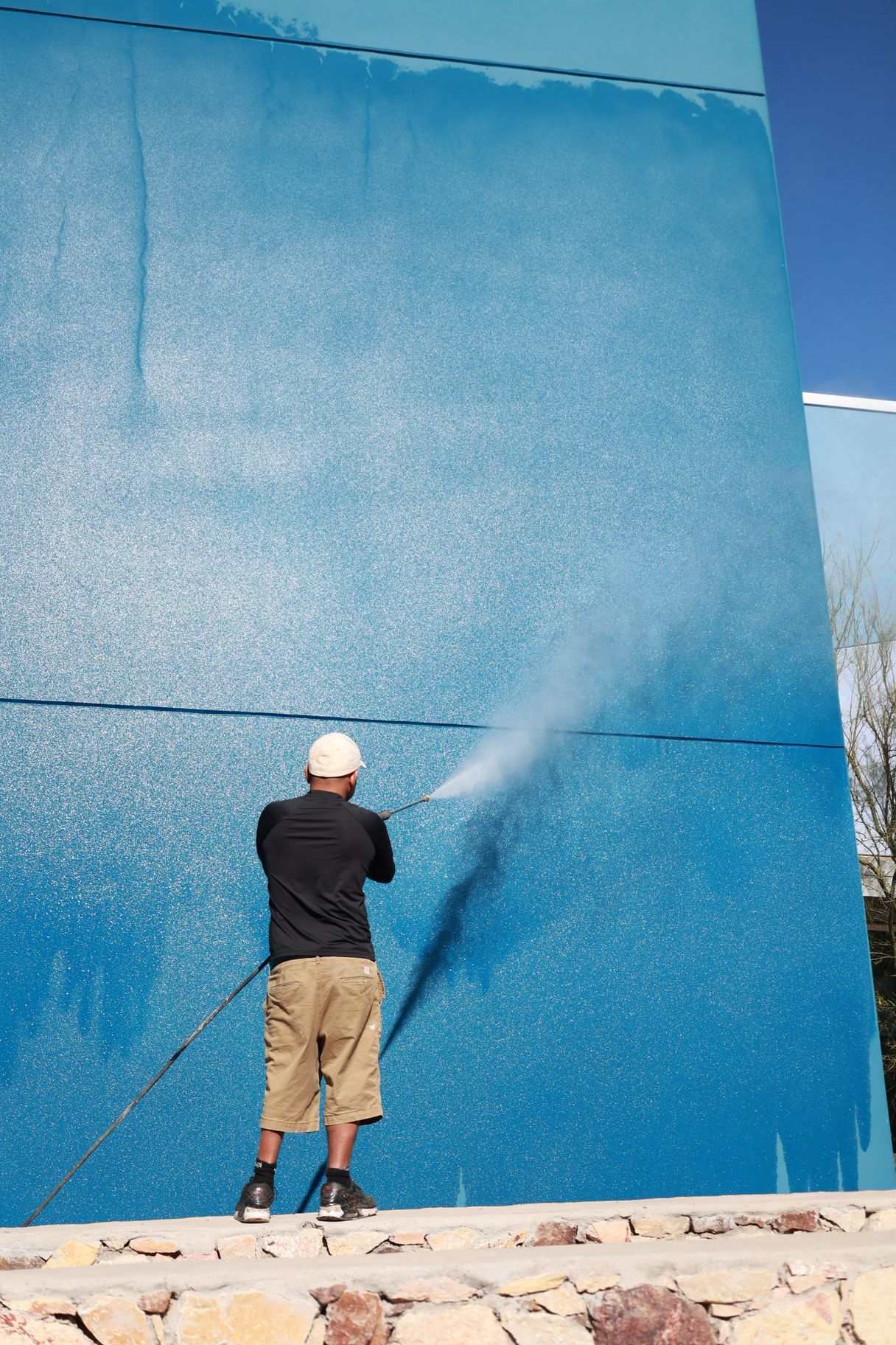 Person power-washing a large blue wall outdoors.