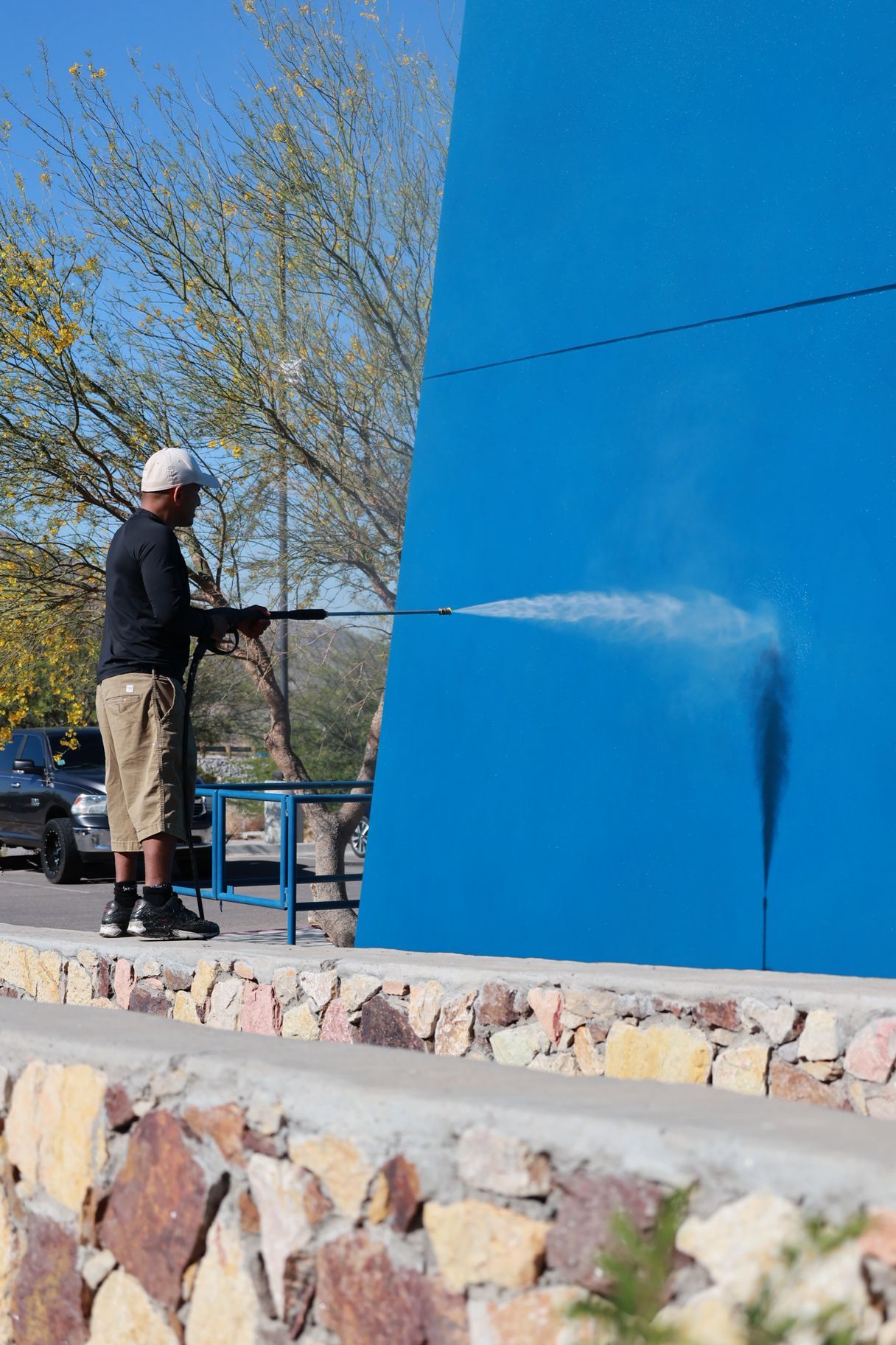 Person pressure-washing a large blue wall outdoors.