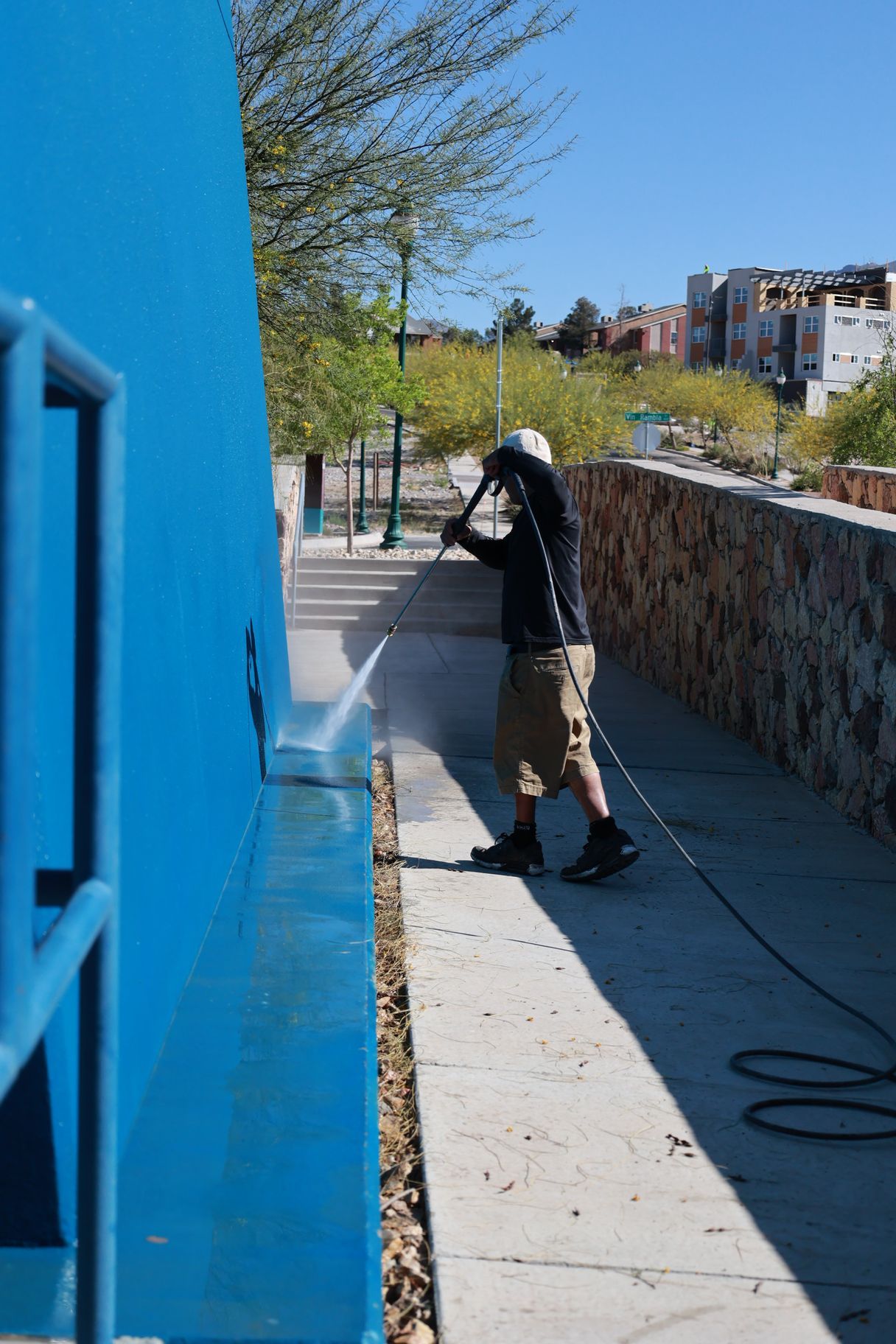 Person pressure-washing a blue wall and sidewalk outdoors on a sunny day