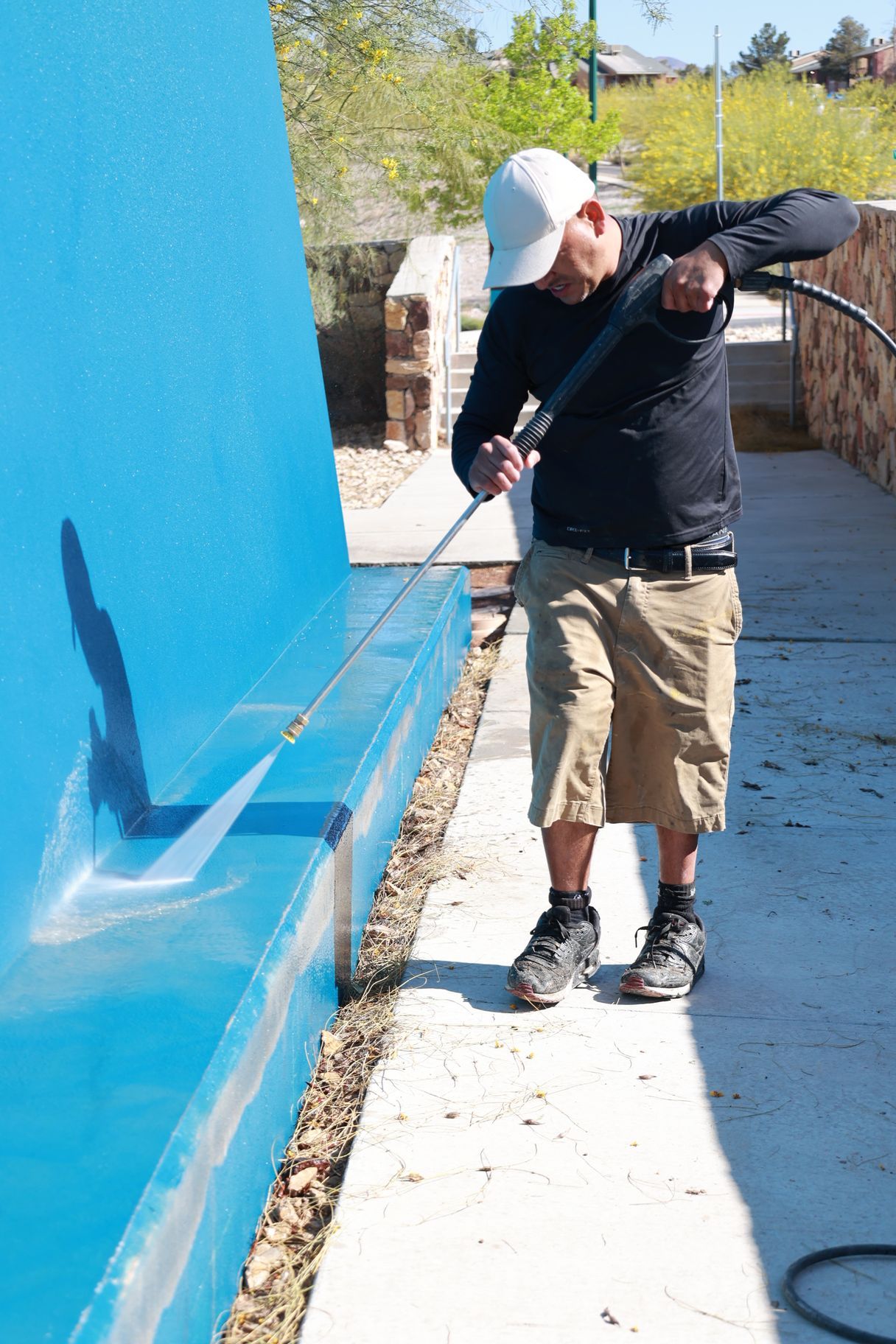 Person painting a bright blue wall outdoors on a sunny walkway