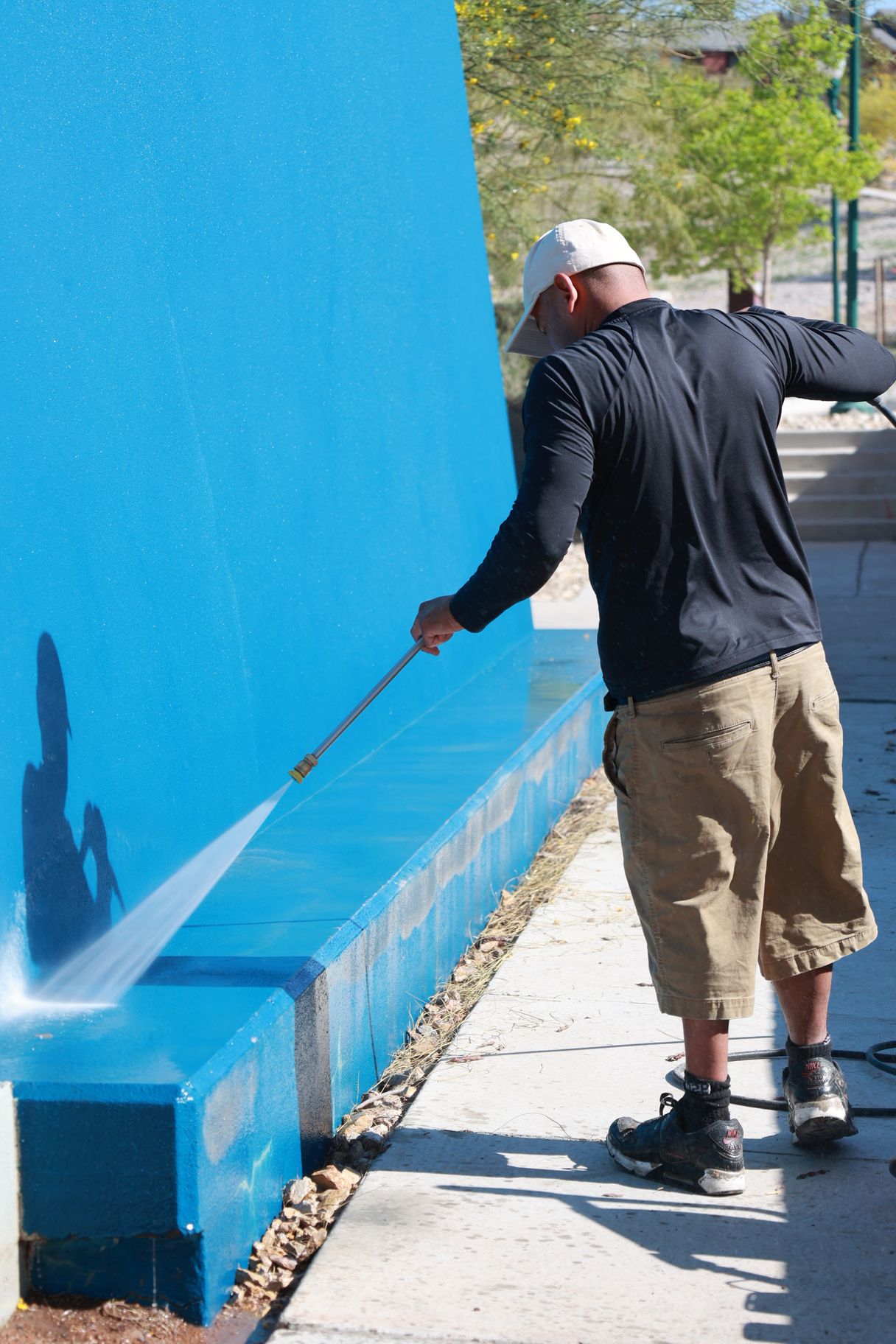 Person power-washing a bright blue wall beside a sidewalk.