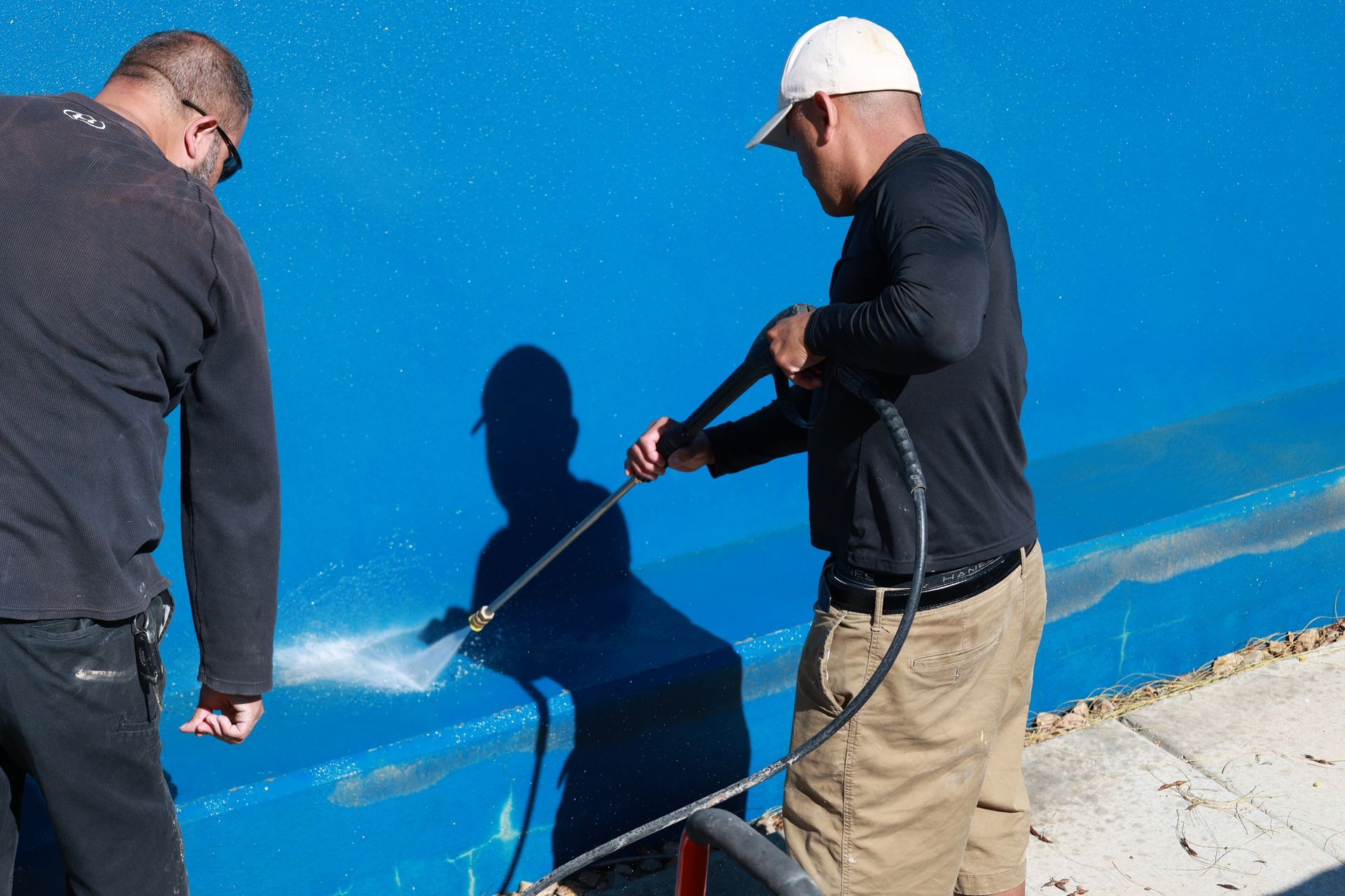 Two workers inspect a blue wall with a measuring tool outdoors.
