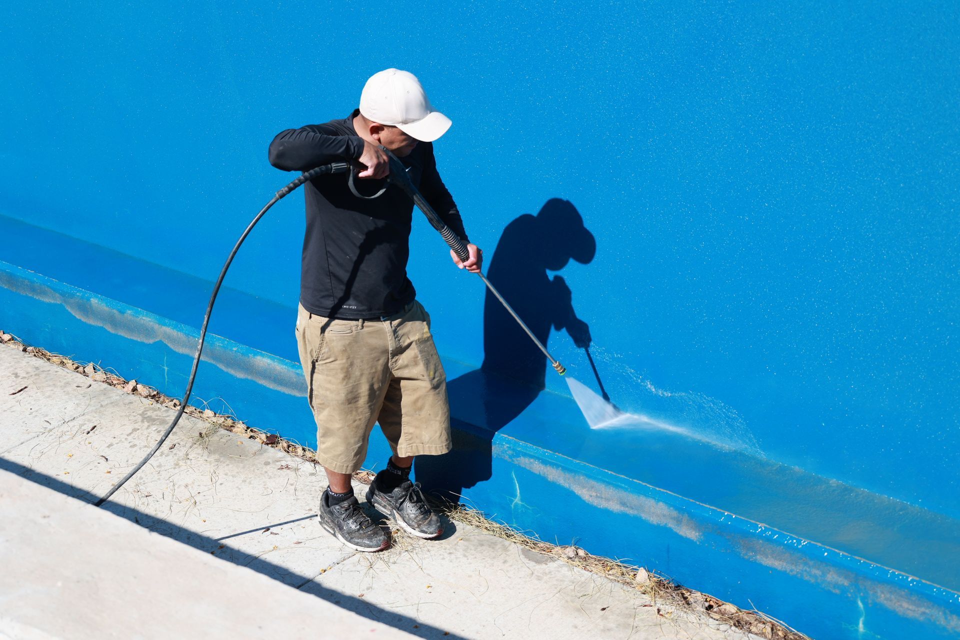 Person in a white hard hat pressure-washing a bright blue wall with a hose.