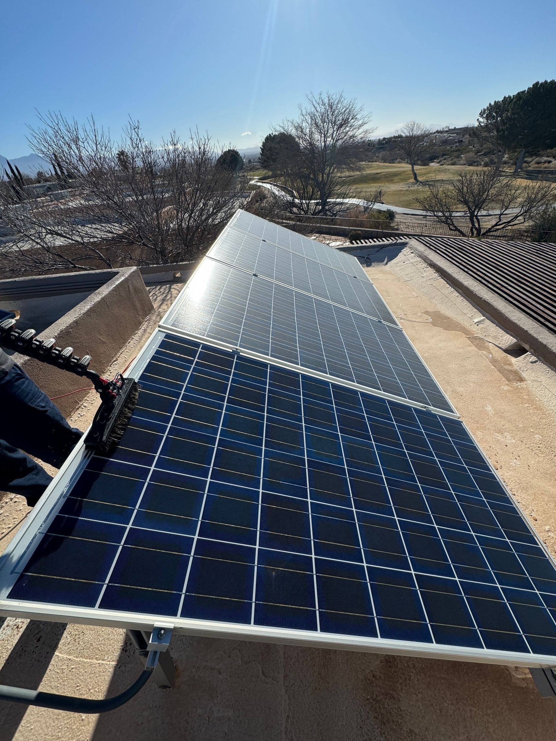 Solar panels installed outdoors on a rooftop, reflecting sunlight in a dry landscape.